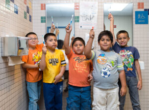 Kids hold toothbrushes in front of a school-based health clinic