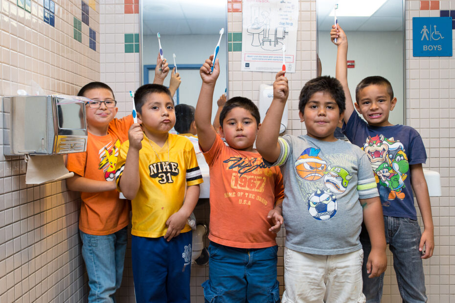 Kids hold toothbrushes in front of a school-based health clinic